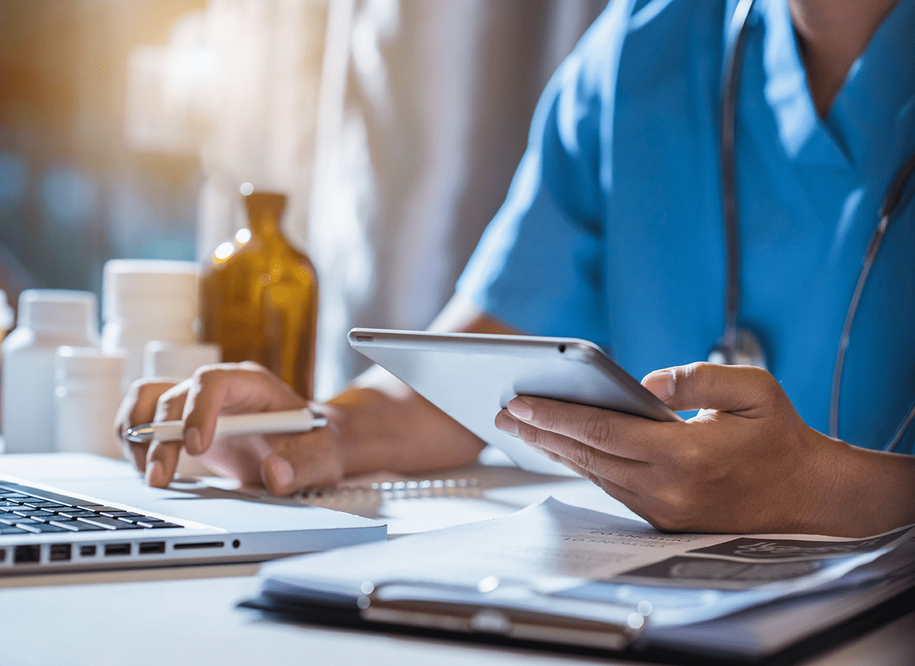 Person in blue overalls holding a tablet and looking at medicines on an office table