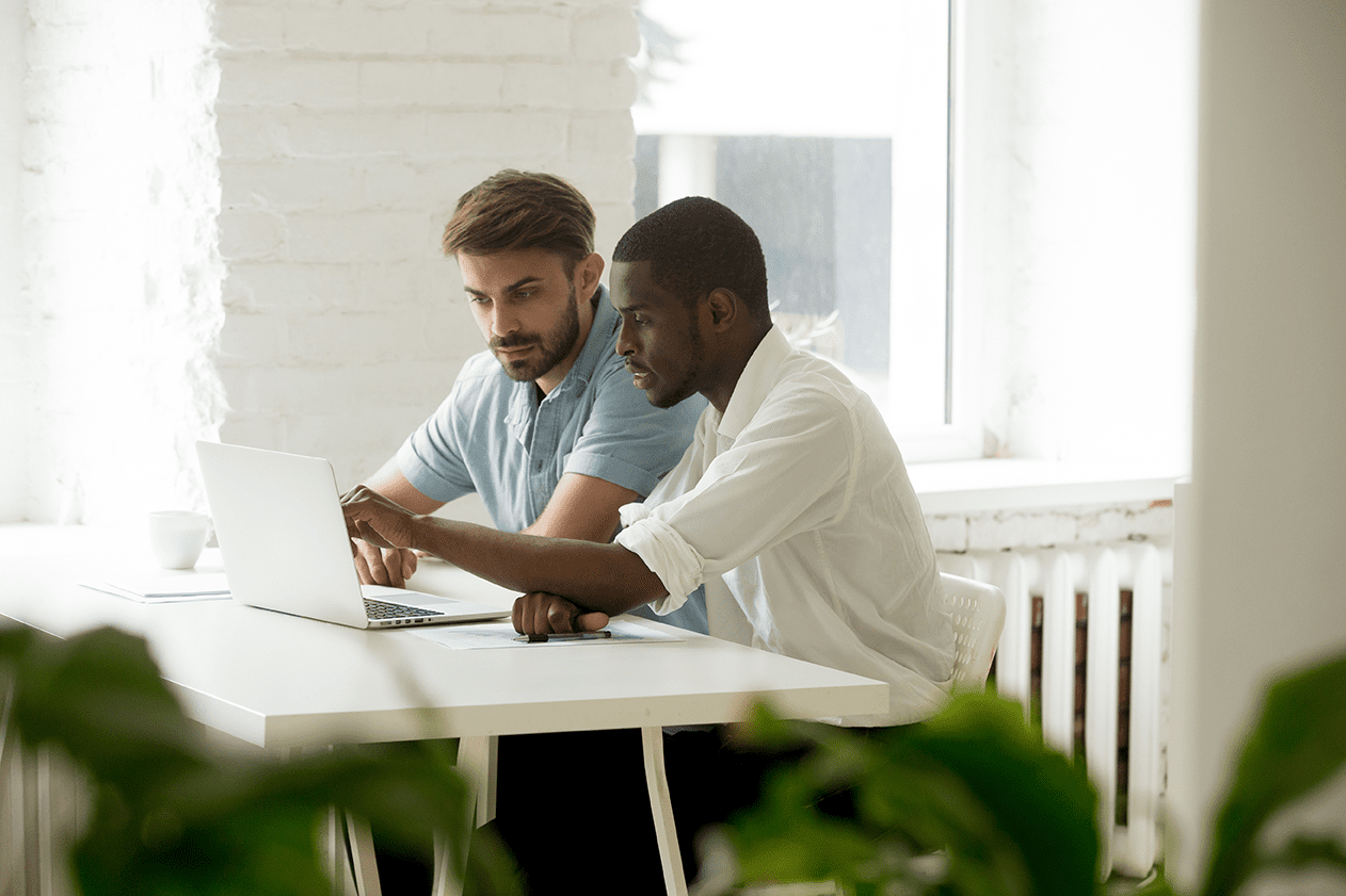 Two people sitting at desk, looking at computer screen